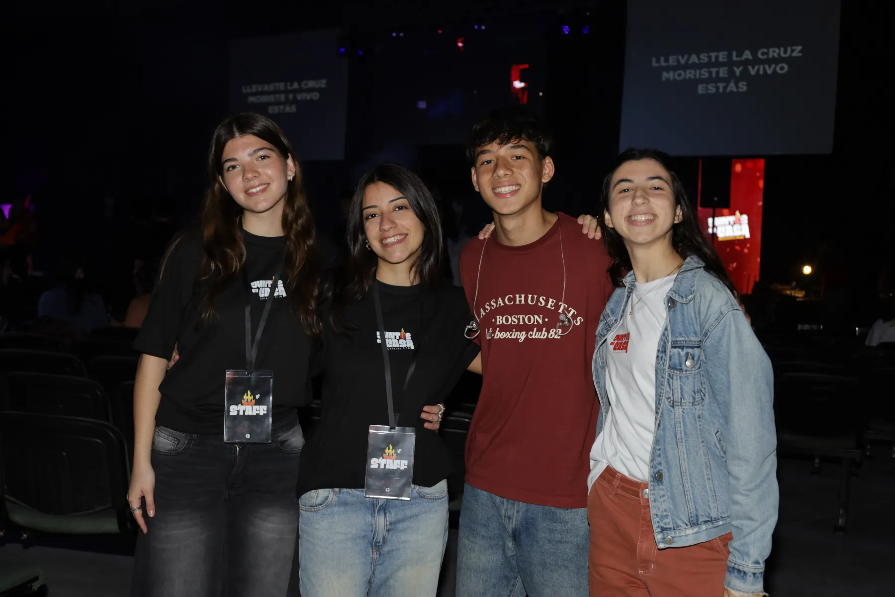 Cuatro jóvenes del staff sonriendo juntos frente al escenario.